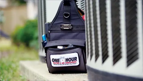 A black One Hour Air Conditioning & Heating utility bag sitting next to a condenser outside a Niceville FL home